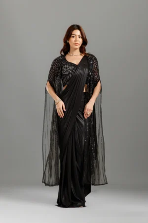 Black Pearll Black Designer Lycra Saree with Embellished Sequin Blouse | Premium Party Wear Saree for WomenTurn heads with the timeless elegance of the Black Pearll Black Designer Lycra Saree, a perfect blend of sophistication and modern glamour. Crafted from premium-quality Lycra fabric, this saree features a graceful fluid drape that enhances your silhouette while ensuring all-day comfort. The highlight of this ensemble is its stunning heavily embellished sequin blouse with intricate beadwork and stylish fringe detailing, adding a luxurious touch to your festive and party wardrobe.  The classic solid black saree paired with the designer blouse creates a chic and elegant look, making it ideal for weddings, receptions, cocktail parties, engagement ceremonies, festive celebrations, anniversary events, evening functions, and special occasions. Whether styled with statement jewellery or minimal accessories, this saree effortlessly delivers a sophisticated and fashionable appearance.  Upgrade your ethnic collection with this premium Black Pearll creation that perfectly combines traditional elegance with contemporary style.